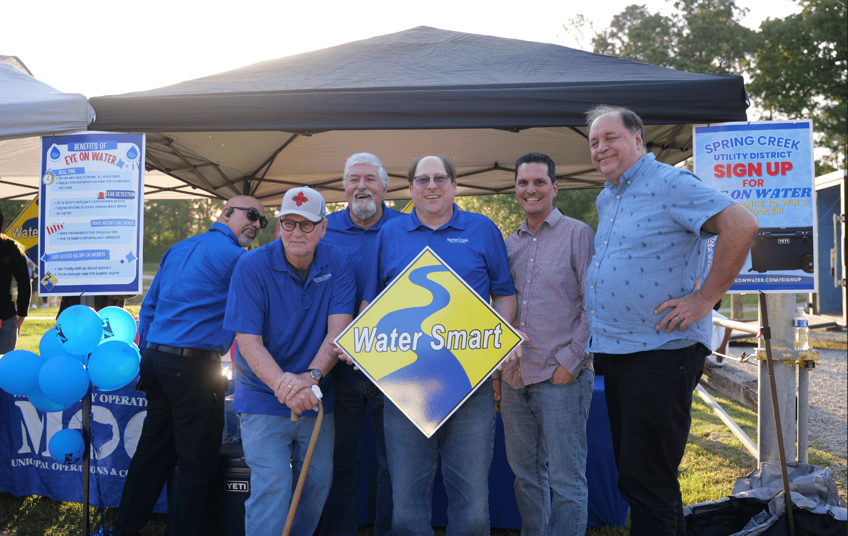 the full board of directors standing together with the water smart sign in front of a tent