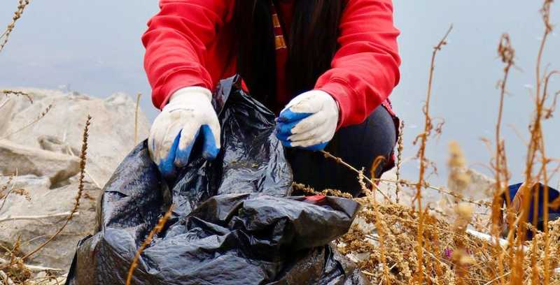 a person wearing a red jacked and gloves putting recyclables into a black bag