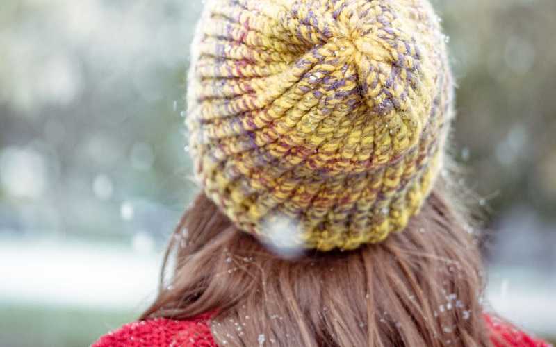 a person with long brown hair and a yellow knit hat in the snow