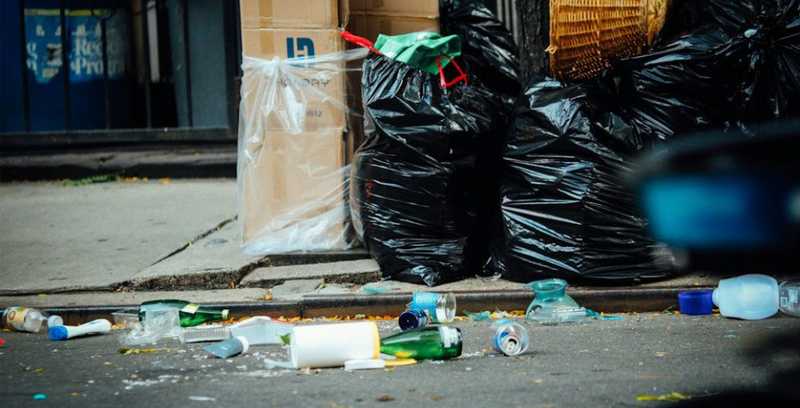 garbage bags lined up along curb with assorted trash littering the street