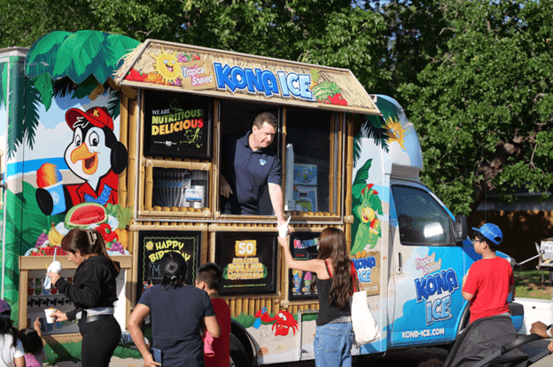 a man in a snow cone truck handing out a cup to a young woman